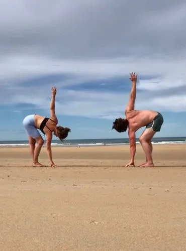 Ein Paar macht gemeinsam Yoga am Strand in einer gespiegelten Haltung